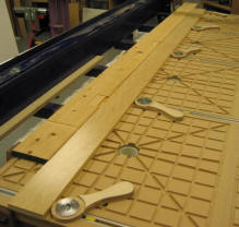 A Cypress door jamb is machined for hinges using cam levers and stops which are bolted to the edge of the table. A plywood strip spreads the clamping pressure, especially at the end where the workpiece doesn’t reach the T-track, but care must be taken not to make the caul too wide or there can be a tendency for the workpiece and caul to “hinge” where they meet and rise off the table.